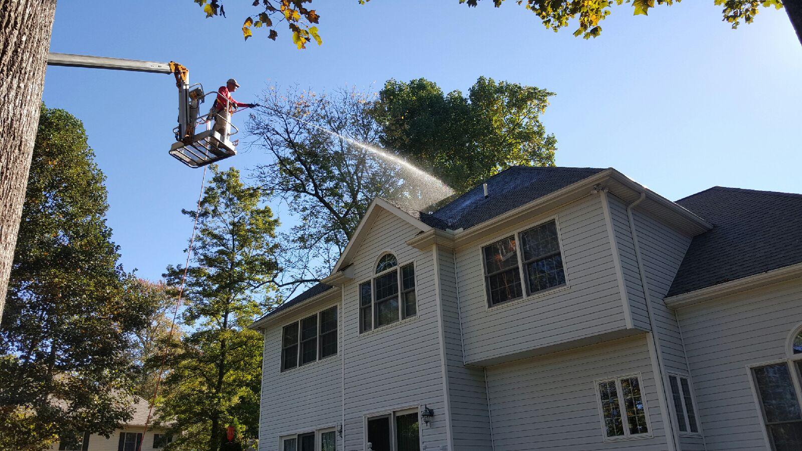 Man on lift above house cleaning algae off roof